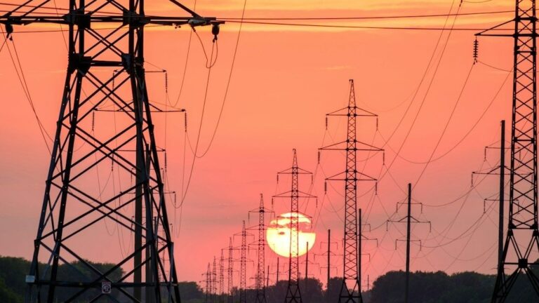 Hoogspanningsmasten en elektriciteitslijnen tegen een oranje avondlucht