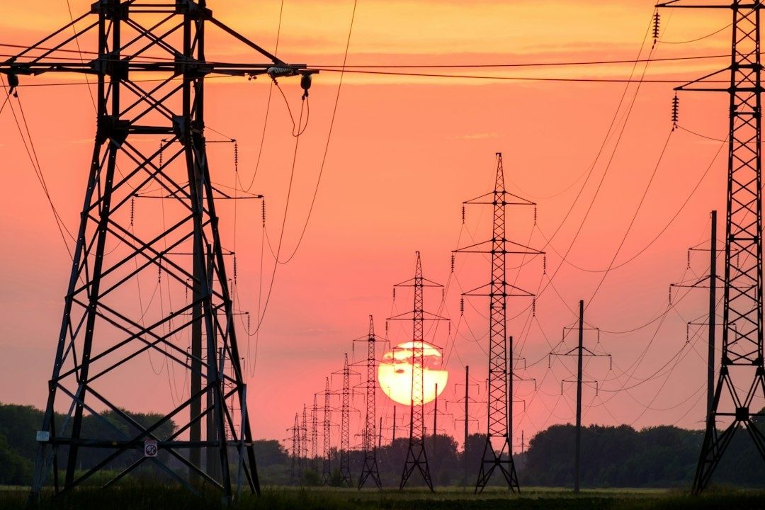 Hoogspanningsmasten en elektriciteitslijnen tegen een oranje avondlucht